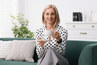 Photo of Smiling middle aged woman with cup of hot drink on sofa at home