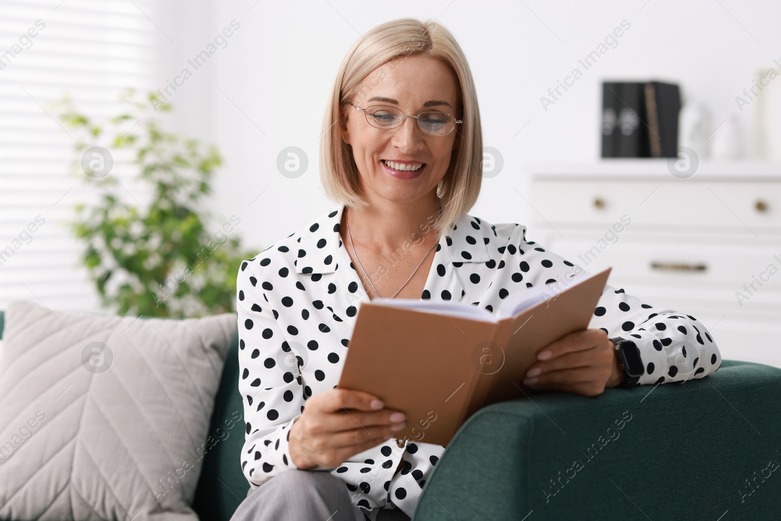 Photo of Portrait of smiling middle aged woman reading book on sofa at home