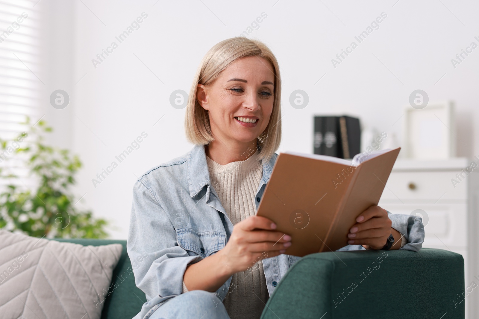 Photo of Portrait of smiling middle aged woman reading book on sofa at home