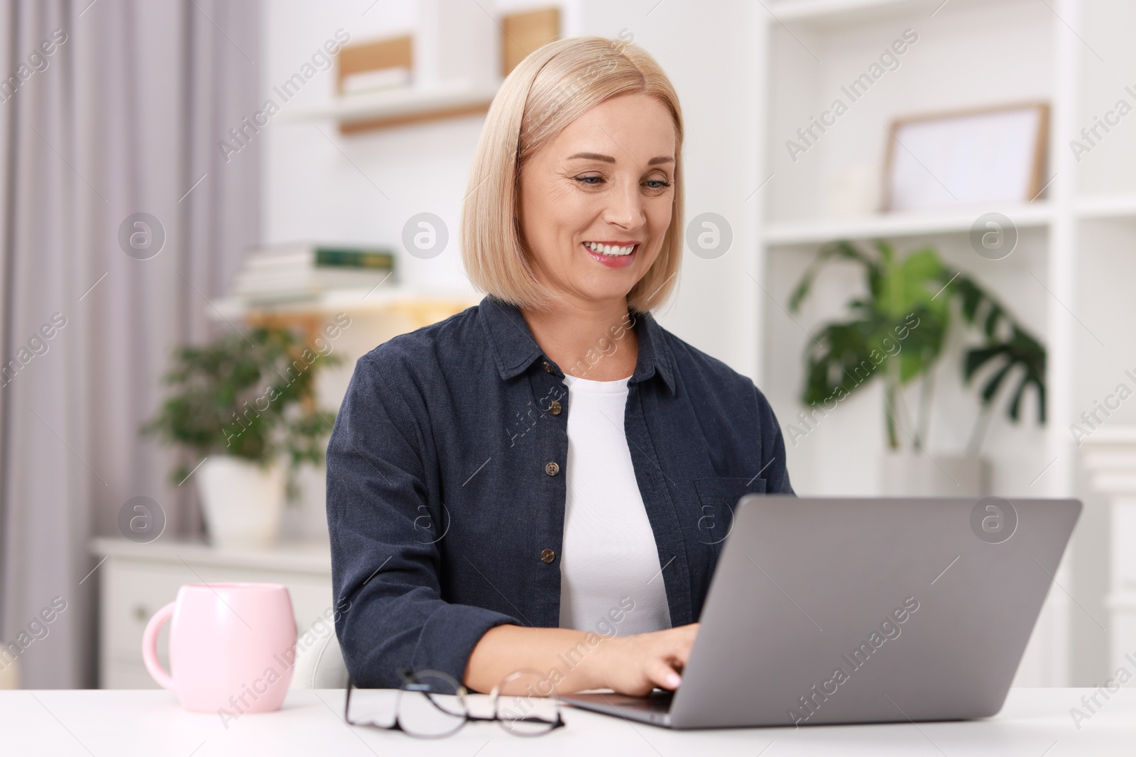 Photo of Portrait of smiling middle aged woman with laptop at table indoors