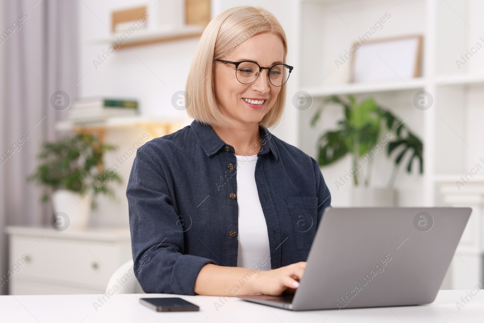 Photo of Portrait of smiling middle aged woman with laptop at table indoors