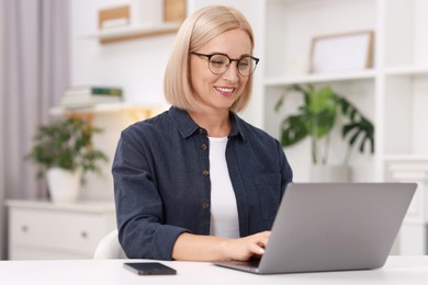 Portrait of smiling middle aged woman with laptop at table indoors