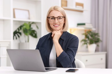 Portrait of smiling middle aged woman with laptop at table indoors