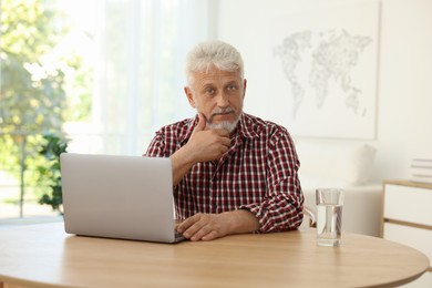 Photo of Senior man with laptop and glass of water at table indoors