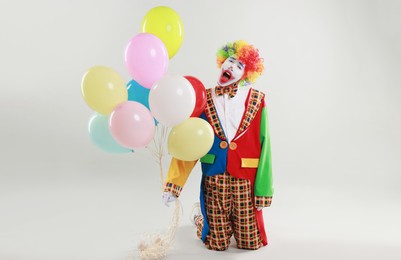 Emotional clown with colorful balloons on light background