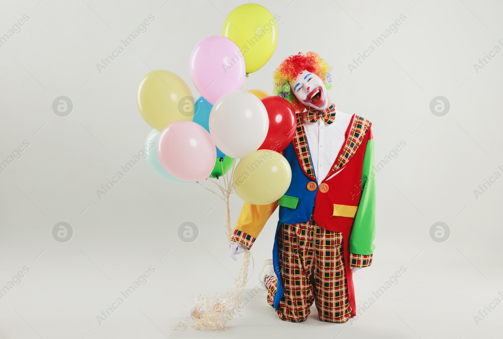 Photo of Happy clown with colorful balloons on light background