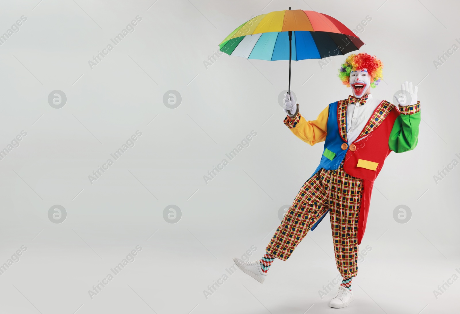 Photo of Happy clown with colorful umbrella on light background