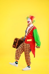 Photo of Happy clown with suitcase on yellow background