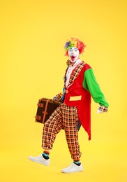 Photo of Emotional clown with suitcase on yellow background