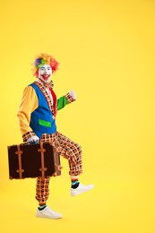 Photo of Happy clown with suitcase on yellow background, space for text