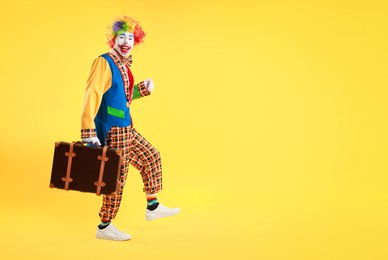 Photo of Happy clown with suitcase on yellow background, space for text