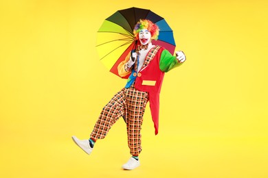 Photo of Emotional clown with colorful umbrella on yellow background