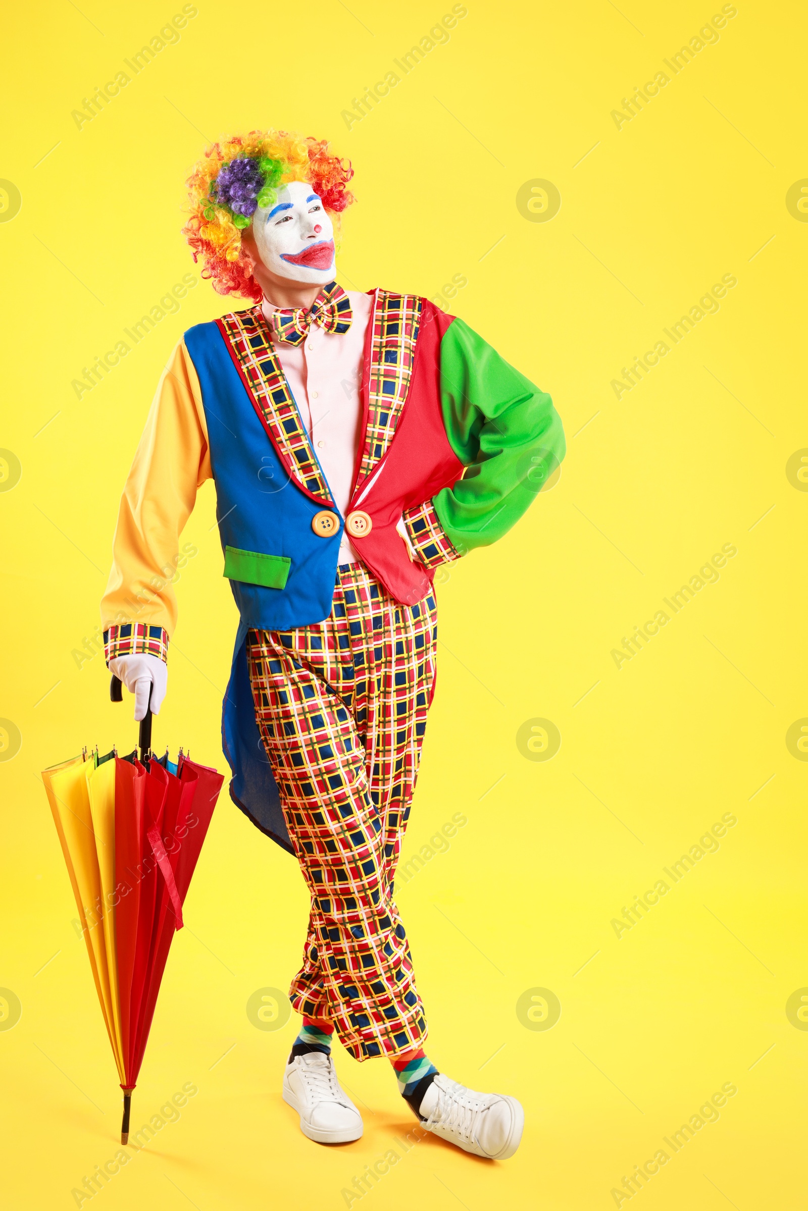 Photo of Clown with colorful umbrella on yellow background