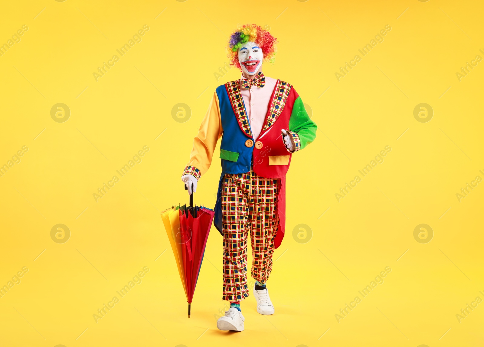 Photo of Happy clown with colorful umbrella on yellow background