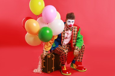 Clown with colorful balloons and suitcase on red background