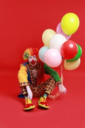 Photo of Happy clown with colorful balloons on red background