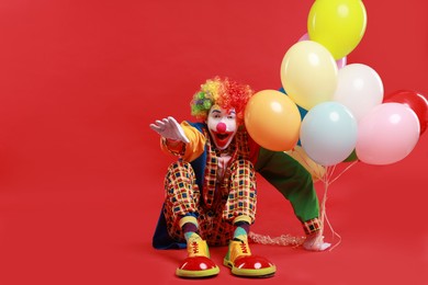 Emotional clown with colorful balloons on red background, space for text