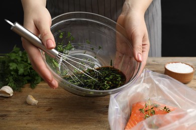 Photo of Woman with soy marinade and salmon fillet in plastic bag at wooden table, closeup