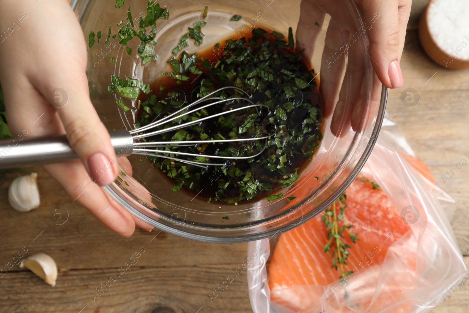 Photo of Woman with soy marinade and salmon fillet in plastic bag at wooden table, top view