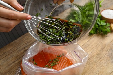 Photo of Woman with soy marinade and salmon fillet in plastic bag at wooden table, closeup