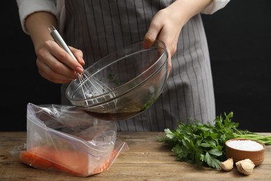 Photo of Woman with soy marinade and salmon fillet in plastic bag at wooden table, closeup