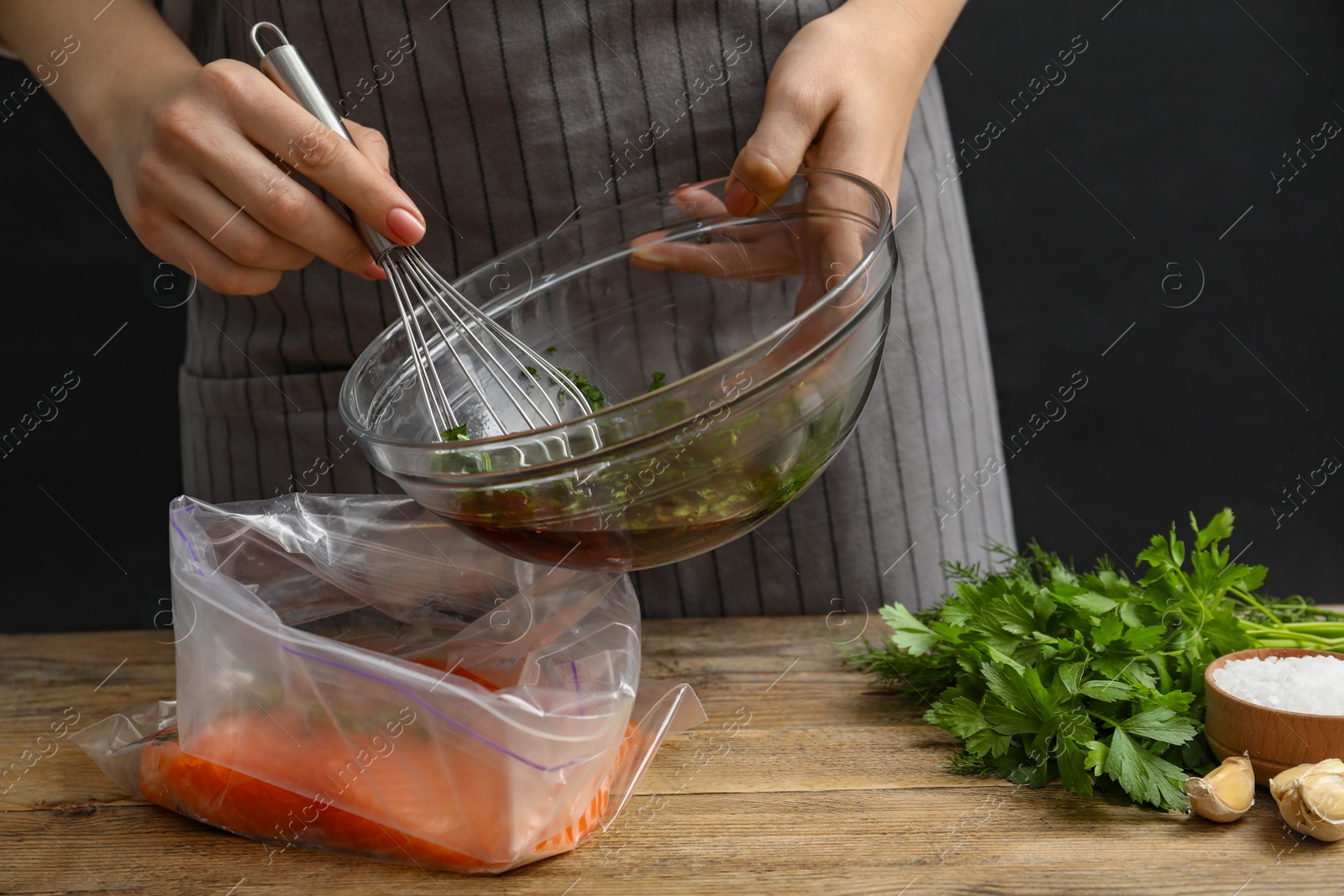 Photo of Woman with soy marinade and salmon fillet in plastic bag at wooden table, closeup