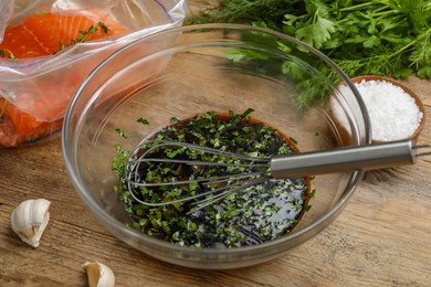 Photo of Soy marinade in bowl, whisk, salmon fillet and spices on wooden table closeup