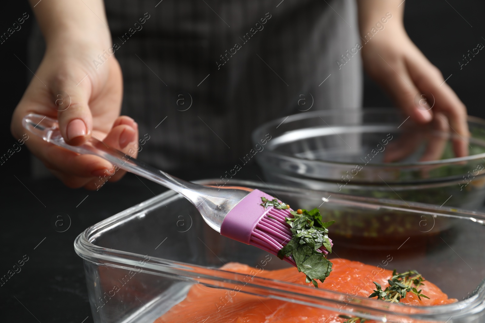 Photo of Woman marinating salmon fillet in dish at table, closeup