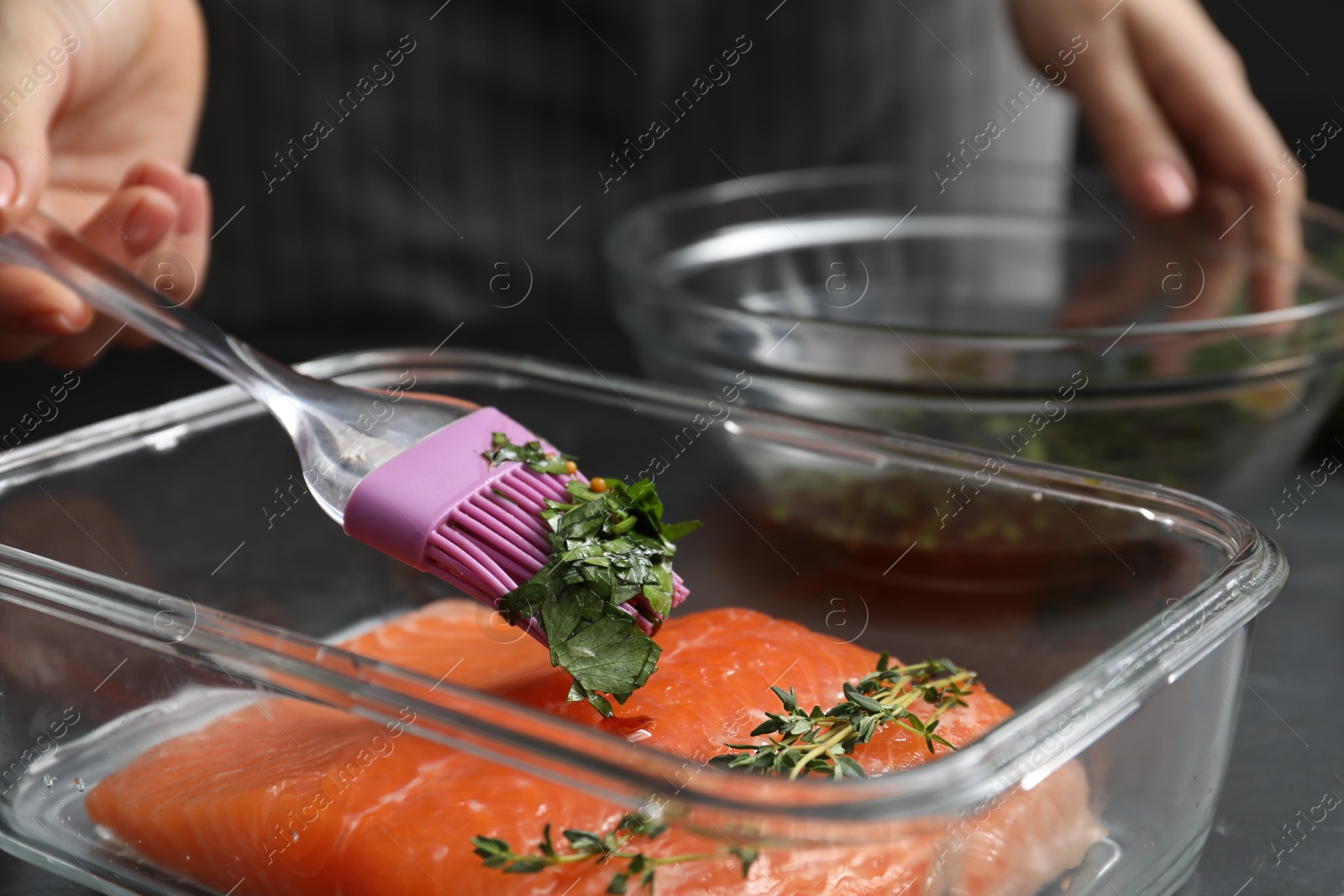 Photo of Woman marinating salmon fillet in dish at table, closeup