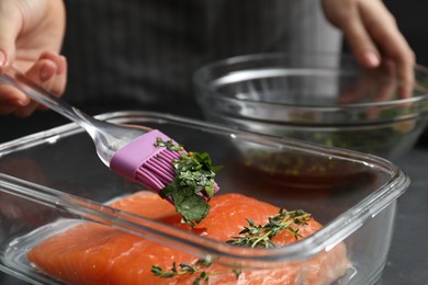 Photo of Woman marinating salmon fillet in dish at table, closeup