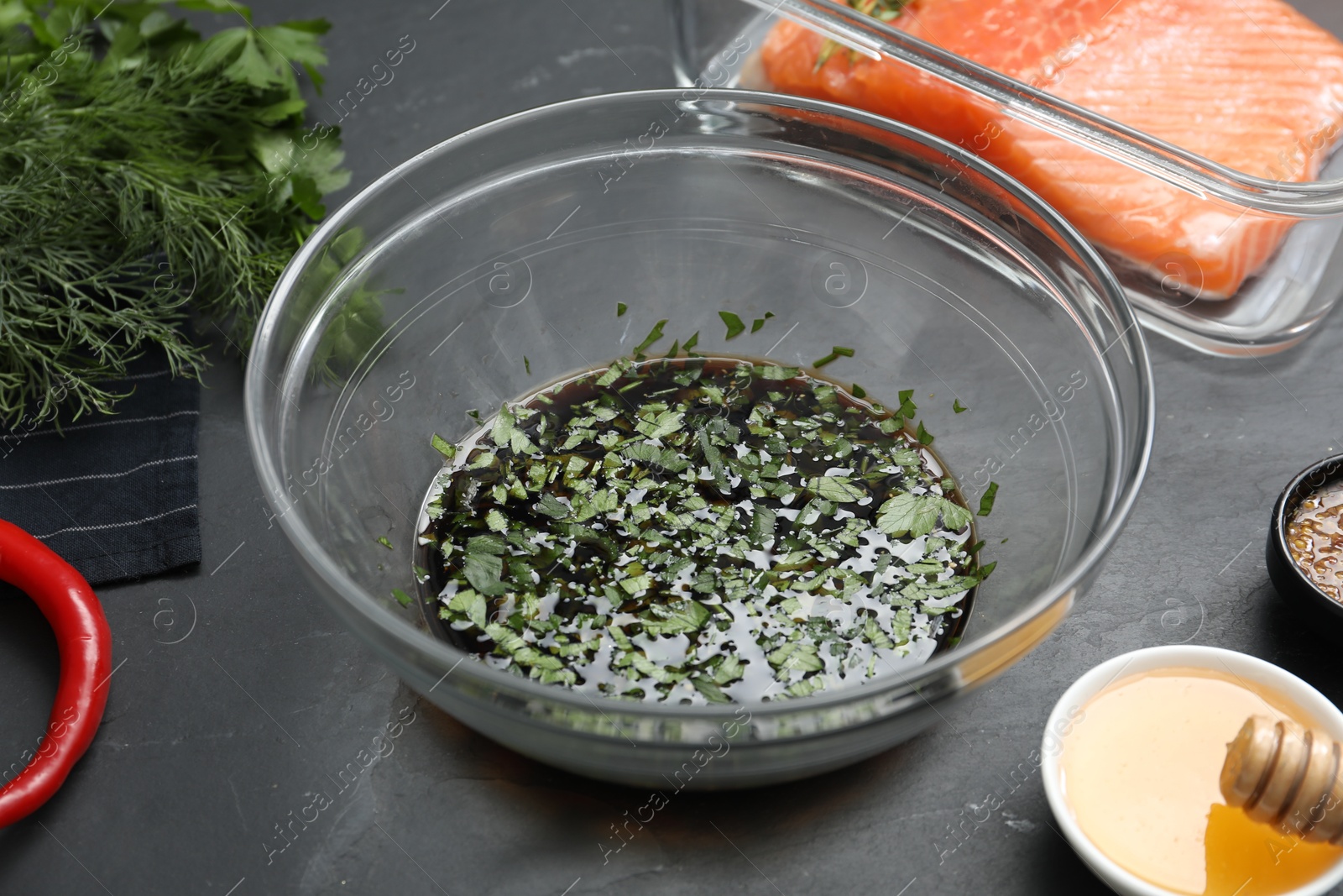 Photo of Soy marinade in bowl, salmon fillet and other products on dark gray textured table, closeup