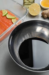 Photo of Soy sauce in bowl, salmon fillet with lime slices, oil, honey and lemon on gray textured table, closeup