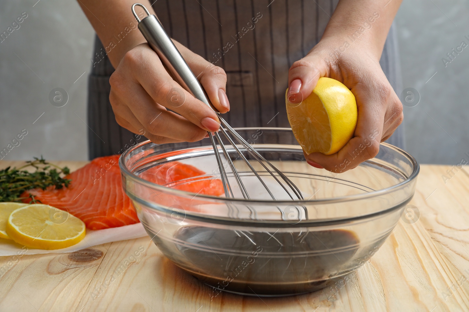 Photo of Woman squeezing lemon juice into bowl with soy sauce at table, closeup