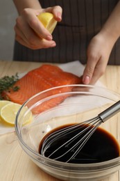 Photo of Woman squeezing lemon juice onto salmon fillet wooden at table, focus on bowl with soy sauce