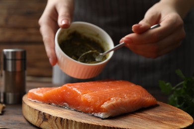 Photo of Woman marinating salmon fillet at wooden table, closeup