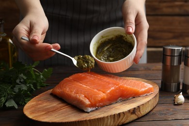 Photo of Woman marinating salmon fillet at wooden table, closeup