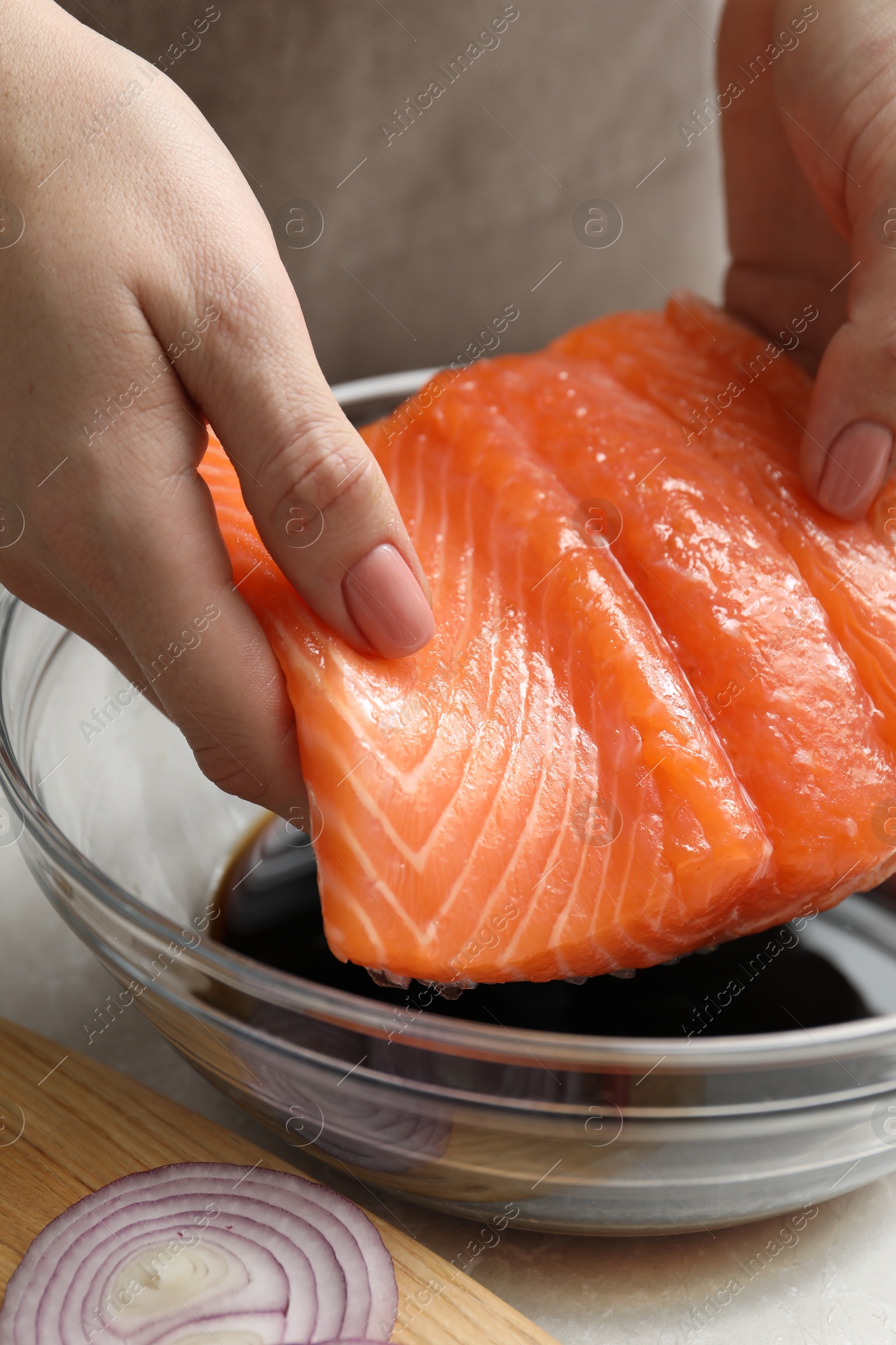 Photo of Woman with salmon fillet and soy sauce at gray table, closeup