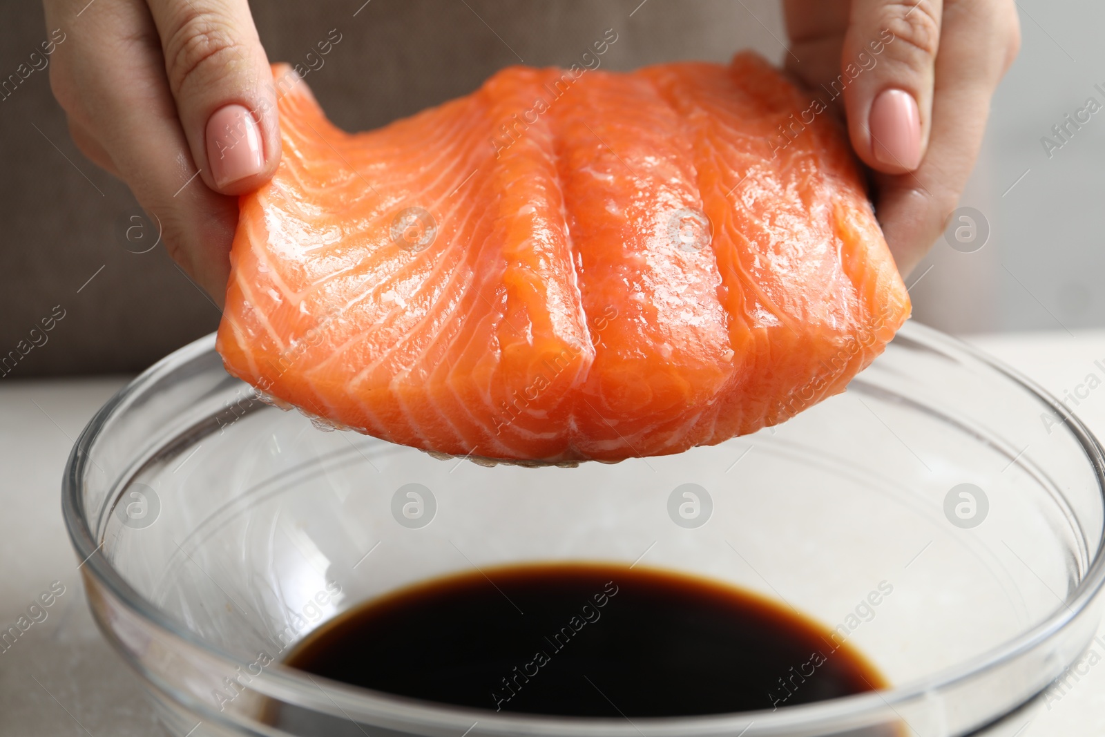 Photo of Woman with salmon fillet and soy sauce at gray table, closeup