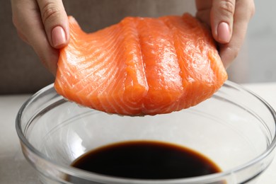 Photo of Woman with salmon fillet and soy sauce at gray table, closeup