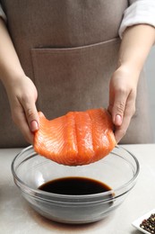 Photo of Woman with salmon fillet and soy sauce at gray table, closeup