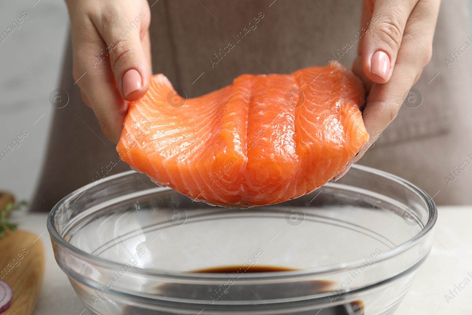 Photo of Woman with salmon fillet and soy sauce at gray table, closeup