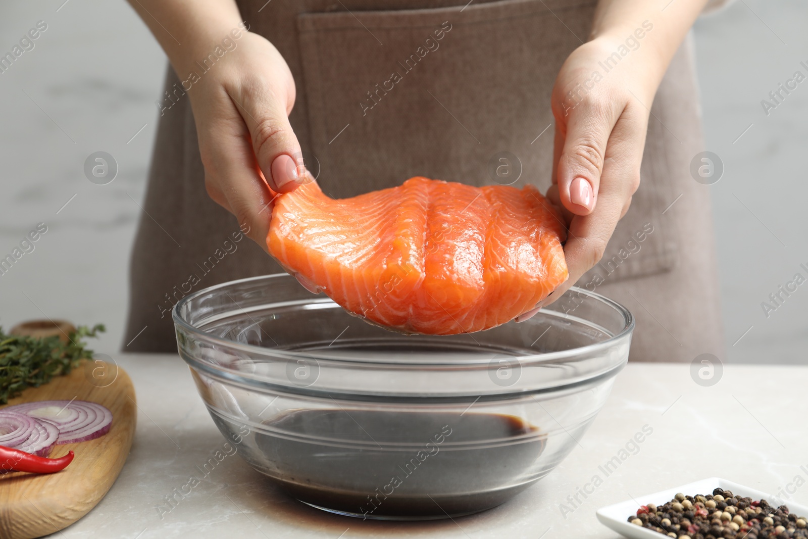 Photo of Woman with salmon fillet and soy sauce at gray table, closeup