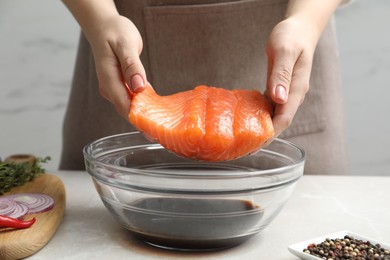 Photo of Woman with salmon fillet and soy sauce at gray table, closeup