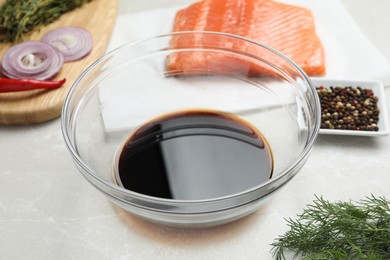 Photo of Soy sauce in bowl, salmon fillet and spices on gray marble table, closeup