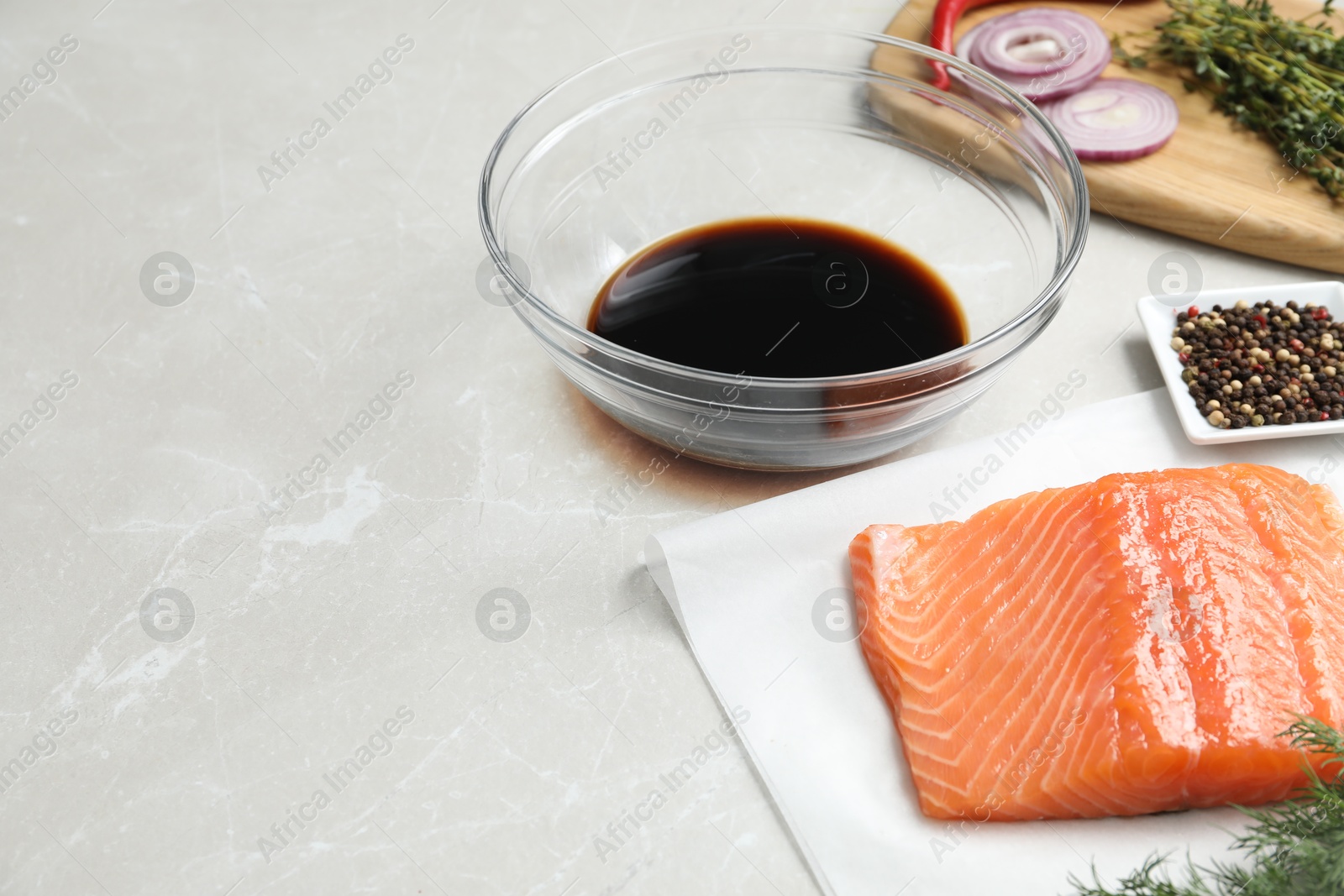 Photo of Soy sauce in bowl, salmon fillet and spices on gray marble table. Space for text