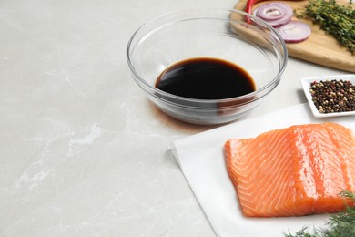 Photo of Soy sauce in bowl, salmon fillet and spices on gray marble table. Space for text