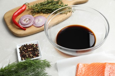 Photo of Soy sauce in bowl, salmon fillet and spices on gray marble table, closeup