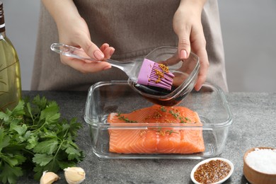 Photo of Woman marinating salmon fillet in dish at gray textured table, closeup