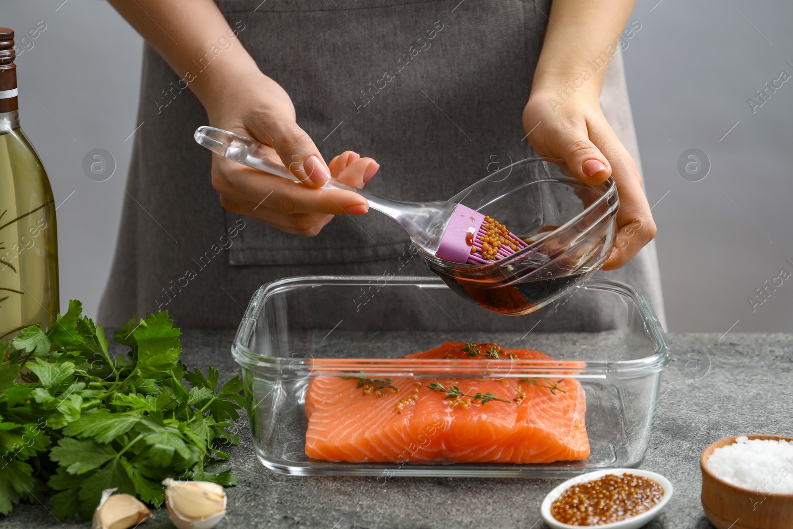 Photo of Woman marinating salmon fillet in dish at gray textured table, closeup