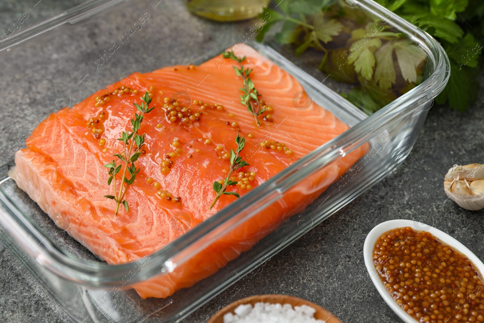 Photo of Salmon fillet with spices in dish on gray textured table, closeup